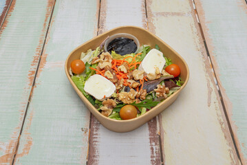 A wonderful salad with walnuts and goat cheese inside a cardboard delivery container