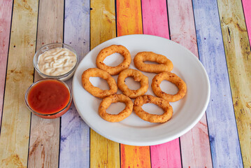 A china plate filled with imitation fried onion rings along with a couple of dipping sauces
