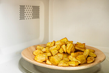 A plate of French fries inside a microwave with a turntable and ventilation grill