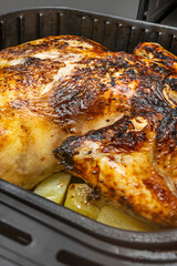 A large roasted chicken with crispy skin along with potatoes and vegetables inside the basket of an air fryer.