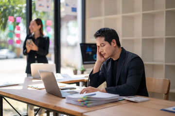 A man is sitting at a desk with a laptop and a stack of papers