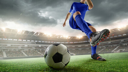 Cropped image of man, soccer player in blue uniform powerfully kicks ball during intense match in stormy weather. 3D stadium. Concept of sport, competition, tournament, strength, motion