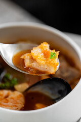 A spoon with shrimp and parsley hovers over a bowl of rich, flavorful seafood soup. The dish is garnished with herbs, showcasing its appetizing and fresh ingredients.