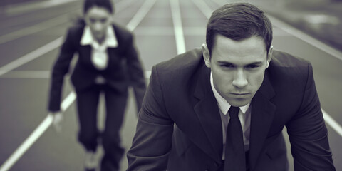 Close-up of a businessman in a suit, ready to start a race, with a blurred businesswoman in the background, symbolizing business competition and ambition
