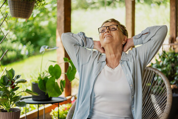 A beautiful senior woman sitting outdoors on a terrace at home in summer.