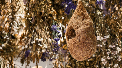 Handcrafted fiber bird nest hanging amidst blurred floral botanical backdrop