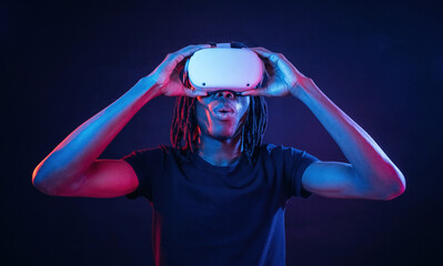 Wow effect, amazed. African American guy is with virtual reality glasses in neon room