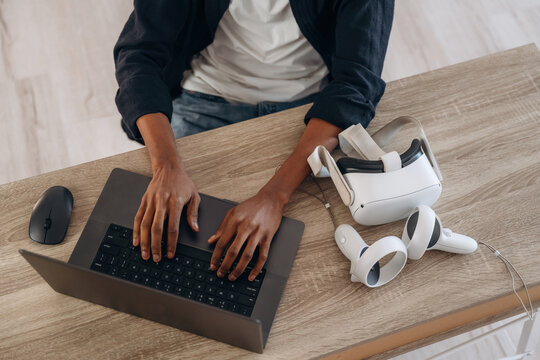 Young man is sitting by table with laptop and virtual reality glasses