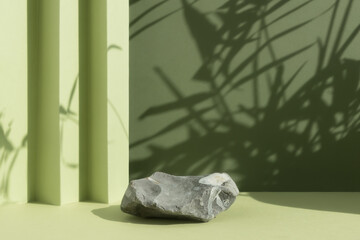 Empty podium made of gray stone on a green background with a shadow of tropical leaves. Scene with a geometric backdrop for the promotion of products, beauty, natural cosmetics. Showcase, display case
