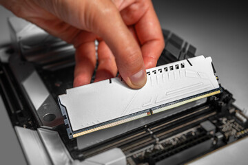 A person is installing a white DDR memory module into a desktop motherboards RAM slot with careful...
