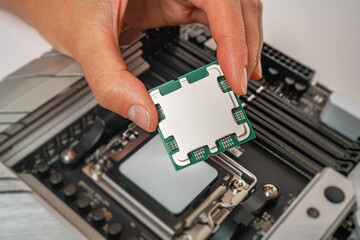 A person is carefully holding a computer processor above a motherboard socket, preparing to install...