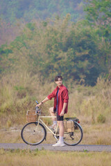 A Handsome young man in a red shirt and black sports shorts is happily riding a white bicycle in...