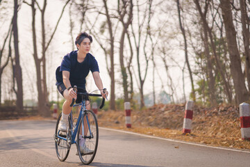Fototapeta premium Handsome young man in a blue shirt and black sports shorts is happily riding a bronze and blue bicycle in the morning for exercise in the park during cold holiday weather. Healthy exercise concept.