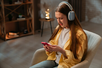 Young teenager girl spending evening time at home, girl sits in chair in the living room and...