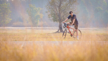 A Handsome young man in a red shirt and black sports shorts is happily riding a red bicycle in the...