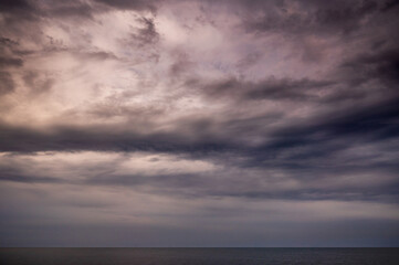 Sun between dark storm clouds over ocean. Dramatic seascape. Clouds and rain flurry over sea.