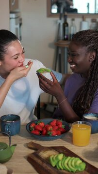 Affectionate lesbian couple enjoys a healthy breakfast together, sharing avocado toast and strawberries