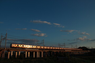 Obraz premium 夕焼け空の下車体を輝かせながら走る武蔵野線E231系電車_2023/6/17撮影