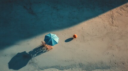 A beach umbrella casts a long shadow on the sand, accompanied by a chair and an orange ball nearby. This tranquil coastal scene captures a moment of relaxation under the sun