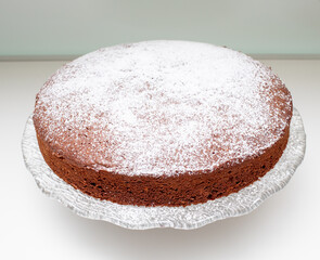 Round caprese cake with icing sugar on glass cake stand