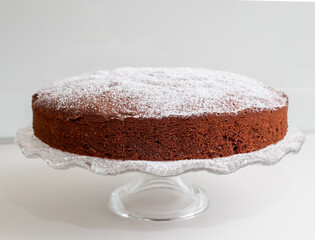 Delicious caprese cake resting on elegant glass cake stand, sprinkled with powdered sugar