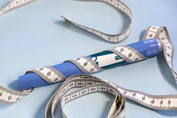 Ozempic syringe pen and measuring tape on blue