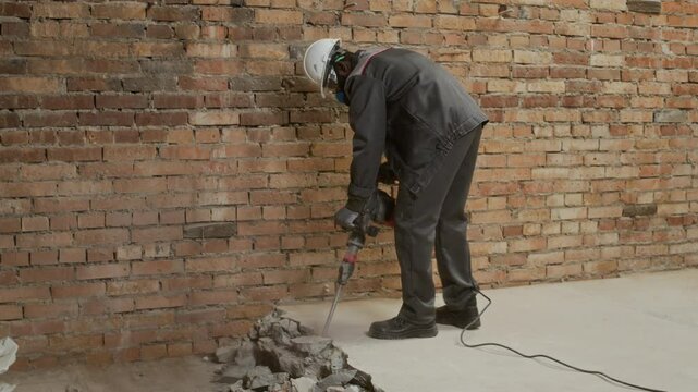 Long copy space shot of African American male laborer in uniform, goggles, respirator and hardhat demolishing floor with jackhammer on worksite