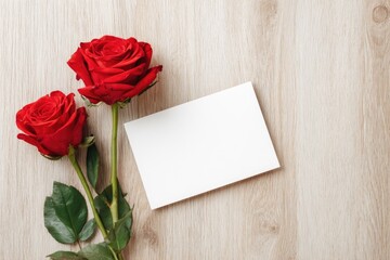 Two red roses and a blank card on a light wood surface