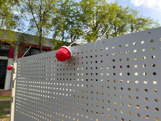 Modern perforated metal fence with red dome lights forms a sleek urban barrier near a contemporary...