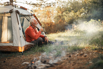 Senior Man Enjoying Tea While Camping in a Forest at Sunset