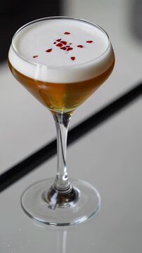 Elegant whiskey cocktail with creamy foam and red garnish drops in tall glass on reflective bar counter. Beverage branding, menu design, bar promotions, nightlife and upscale mixology campaigns. Verti