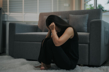 Obraz premium Depressed and unhappy Asian woman sits with anxiety on the sofa in her living room at home.
