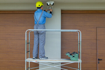 Image of an electrician on a scaffolding while assembling a video surveillance system. External electrical system of a house.
