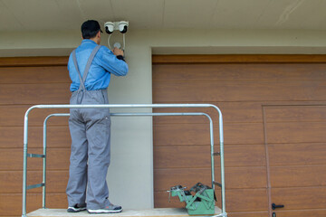Image of an electrician on a scaffolding while assembling a video surveillance system. External electrical system of a house.