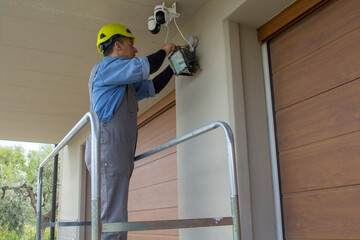 Image of an electrician on a scaffolding while assembling a video surveillance system. External electrical system of a house.
