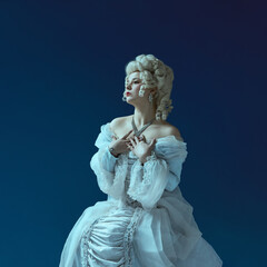 Naklejka premium Dramatic silence. Noblewoman in powdered wig and vintage blue gown holding hands to chest. Concept of emotional intensity, elegance, historic symbolism, fashion, aristocratic femininity.