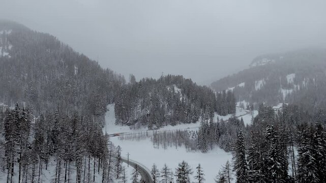 A drone reveals a alpine road, in a dense forest valley in Graub&uuml;nden, Switzerland, shrouded in winter mist.