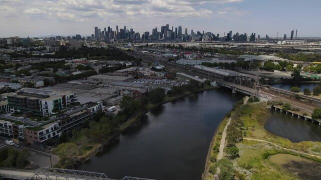 Aerial drone over Maribyrnong river, moving towards Melbourne skyline above rail tracks