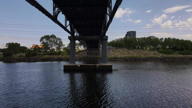 Aerial drone flies under bridge over river in Footscray, Melbourne, cinematic view