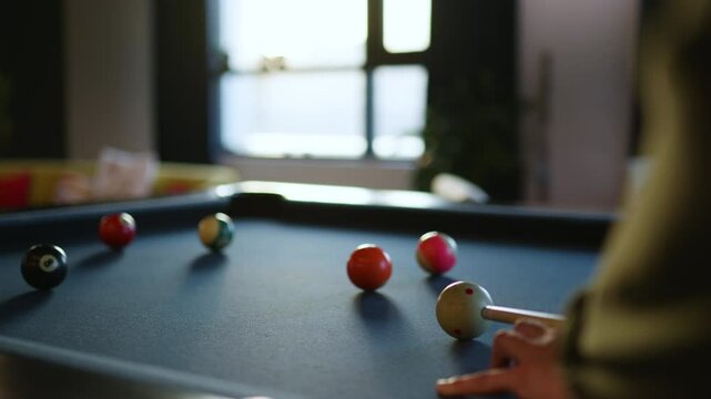 A person enjoys a game of billiards in a modern lounge. Colorful balls are arranged on a pool table, illuminated by warm afternoon light. Comfortable seating surrounds the area. - Powered by Adobe