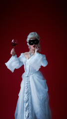 Fototapeta premium Whimsical duchess. Young woman in rococo dress with glass of red wine and black mask expressing surprise. Concept of masquerade, mystery, historical drama, irony, femininity, medieval fashion.