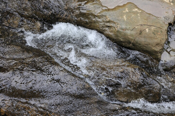 Top Down View Of Crystal Clear Water From A Mountain Stream Cascading Over Smooth, Wet Rocks. Natural Texture Of Flowing Water And Stone. Serene Forest Creek.