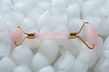 Pink face roller scraping for aesthetic facial massage on ice cubes and water background. Selfcare...