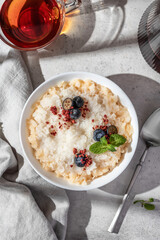 Rice porridge with blueberries, dried raspberries and caramel sauce on a table, hot and healthy breakfast with tea. Bright morning light
