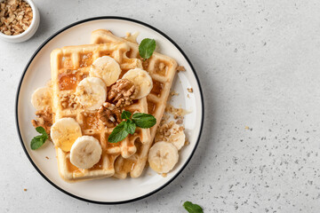 Banana honey belgian waffles on plate served with nuts and mint. Top view. Sweet breakfast with copy space