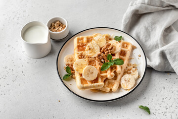 Banana honey belgian waffles on plate served with nuts and mint on white table background. Sweet breakfast with copy space