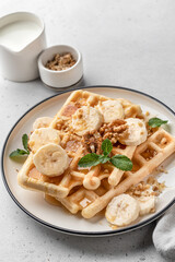 Banana honey belgian waffles on plate served with nuts and mint on white table background. Sweet breakfast close up