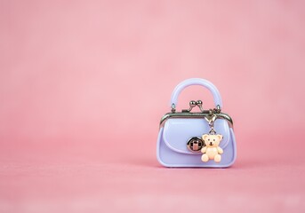 Pastel purple mini handbag with teddy bear charm on pink background