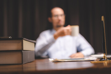 Fototapeta premium Blurred businessman thinking and stressed at desk with documents, coffee cup, and laptop, representing financial problems, business failure, decision-making challenges, and workplace pressure