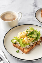 Scrambled eggs on grilled toast with salad leaves, cheese and micro greens on plate on white marble background close up. Delicious healthy breakfast